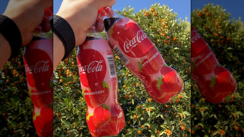 Two bottles of Coca-Cola Strawberry being held up in the sunlight.