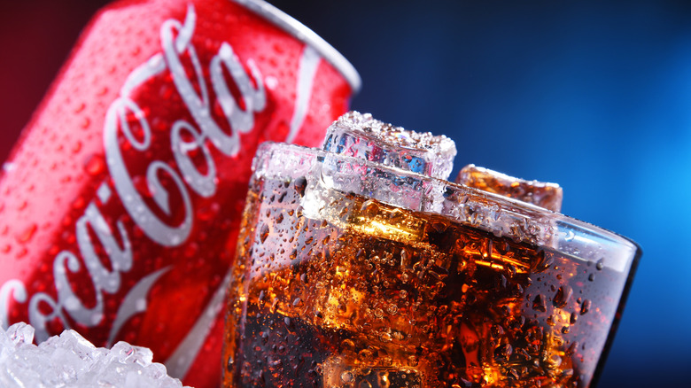 A glass of Coke with ice, next to a sweating can.