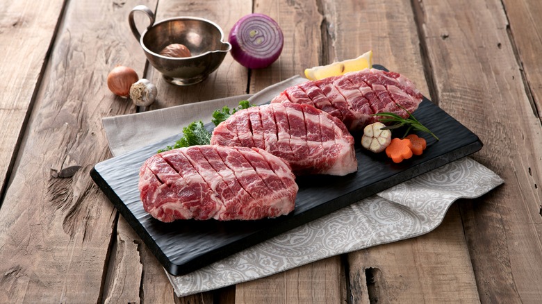 Three Ibérico pork steaks on a black wooden board