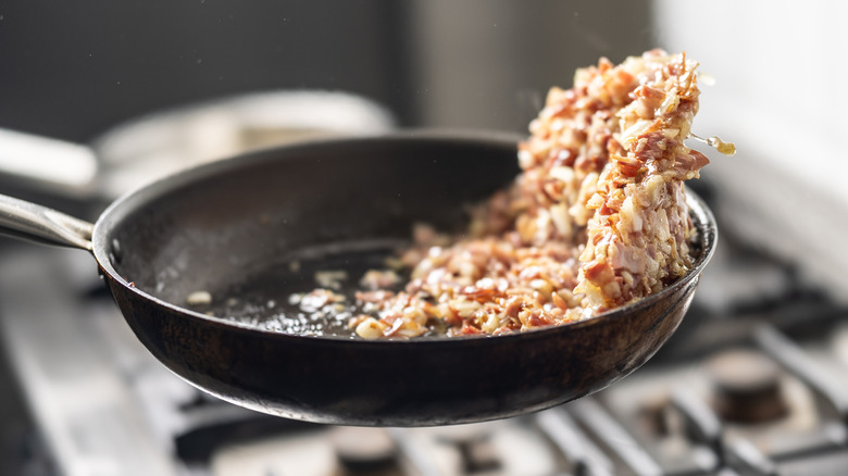 Bacon and onions being flipped in pan