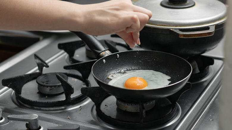 Person sprinkling salt onto egg in frying pan