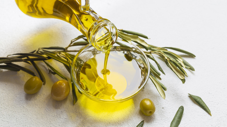Olive oil being poured into bowl, with olives around it