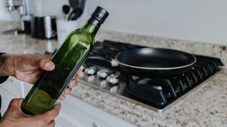 Person holding bottle of olive oil in front of stove