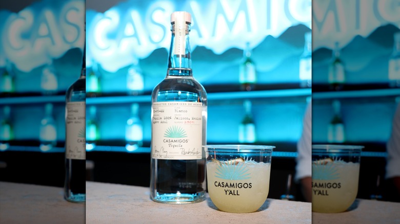 A bottle of Casamigos blanco tequila on a bar top next to a margarita