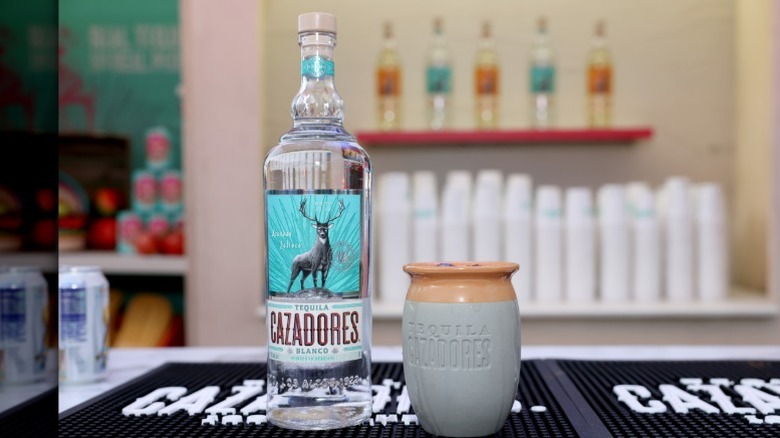 A bottle of Cazadores tequila on a bar next to a branded clay cup