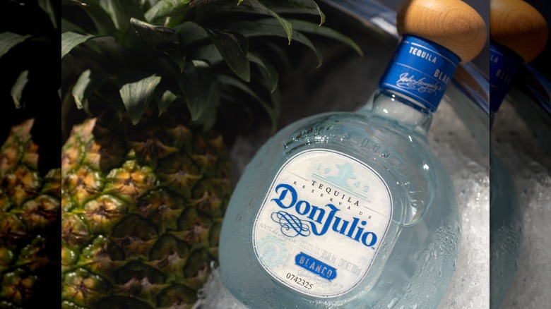 A bottle of Don Julio Blanco tequila resting in ice next to a pineapple