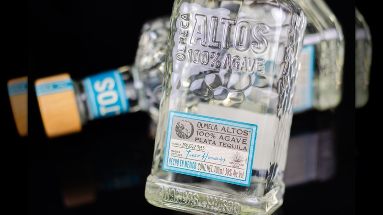 A bottle of Olmeca Altos tequila with a bottle on its side behind it