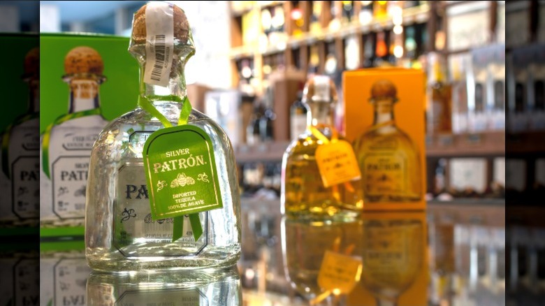 A bottle of Patron Silver tequila on a mirrored table with an anejo bottle behind it