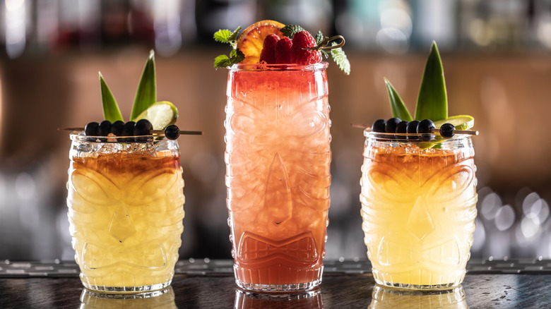 Three mai tai cocktails on a bar with different garnishes