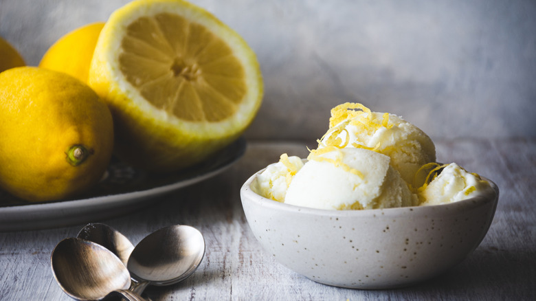A bowl of homemade lemon ice cream with spoons and lemons