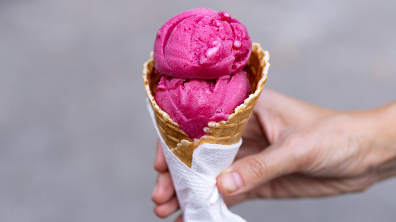 A hand holding an ice cream cone with redcurrant ice cream