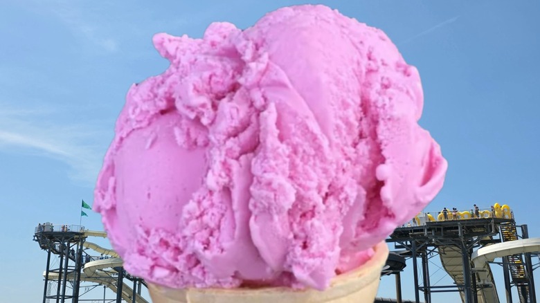 Close-up of pink teaberry ice cream in a cone against backdrop of an amusement park
