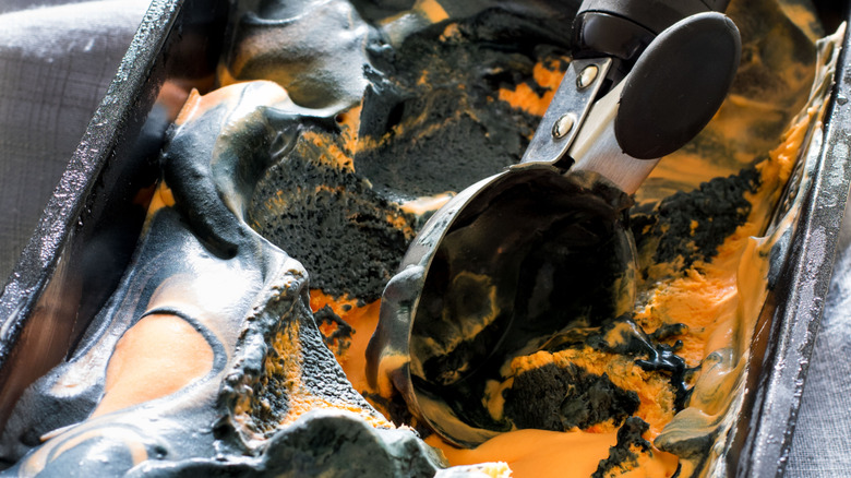 Ice cream scoop lying in container of orange and black tiger tail ice cream