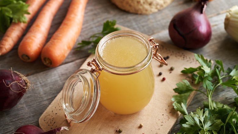 glass jar of clear chicken consomme surrounded by fresh ingredients