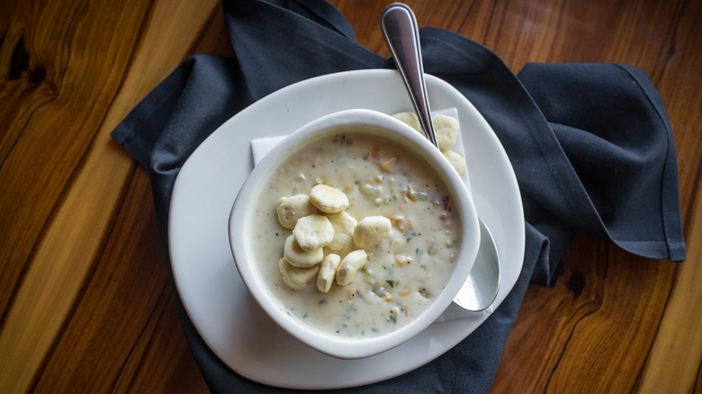 overhead shot of a bowl of creamy chowder topped with oyster crackers styled on a table with spoon and napkin