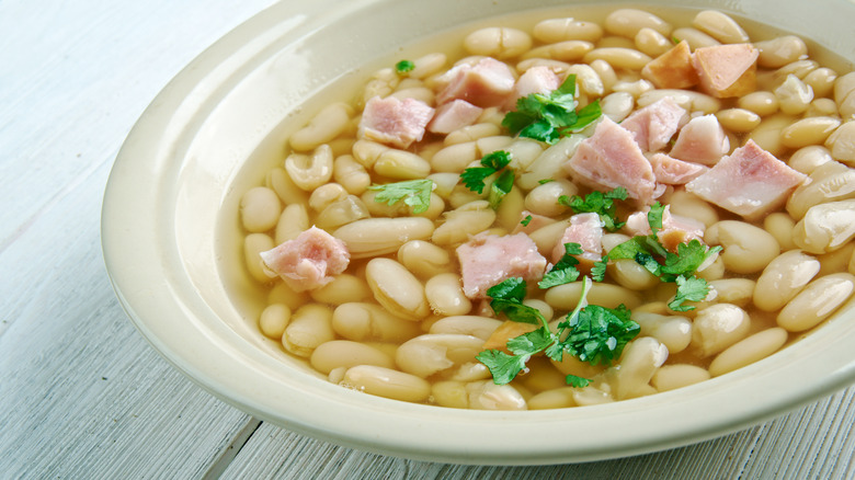 bowl of senate bean soup, topped with diced ham and parsley, on white wood table
