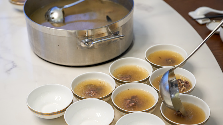turtle soup being ladled into small white bowls, with a large pot of soup in the background