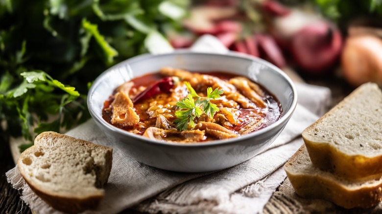 bowl of spicy beef tripe soup styled with bread and fresh vegetables on a table