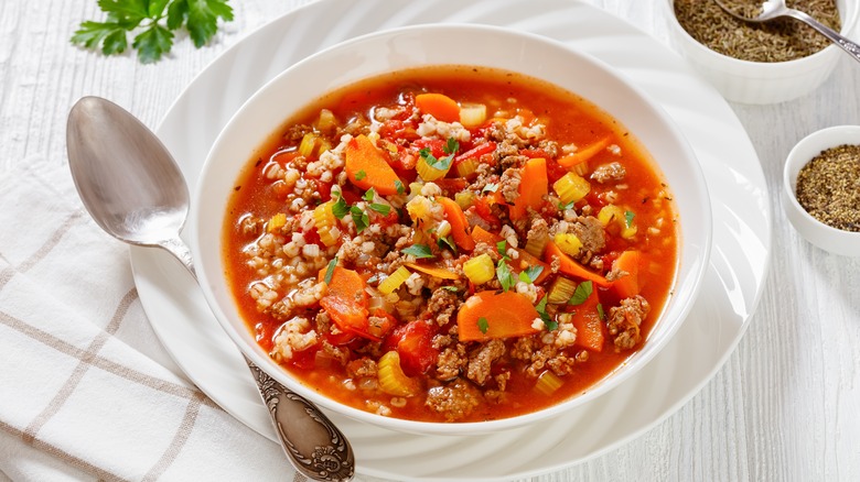 bowl of hamburger soup on white table surrounded by small bowls of seasonings