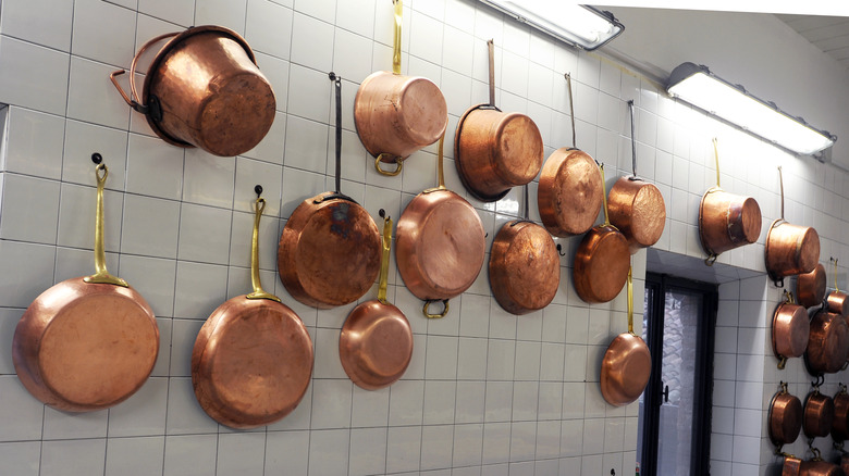 copper pots and pans hanging on a tiled wall in a restaurant kitchen