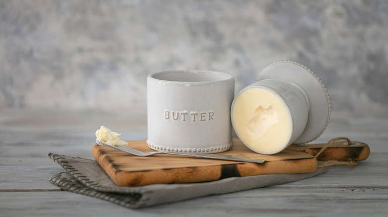 a butter bell opened to reveal butter inside, styled on a wood cutting board against grey background