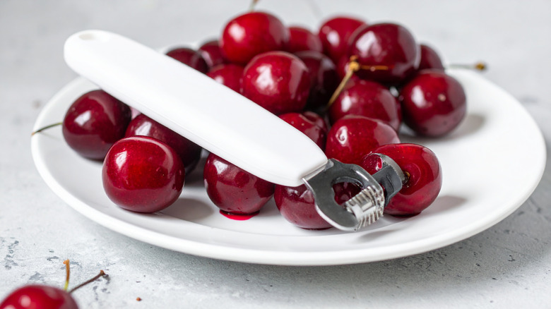 red cherries on a white plate with a cherry pitter