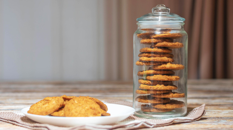 plate of cookies next to glass cookie jar against neutral background