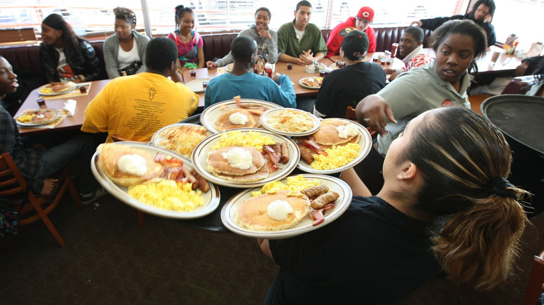 Denny's server hold multiple plates of breakfasts in a crowded Denny's restaurant