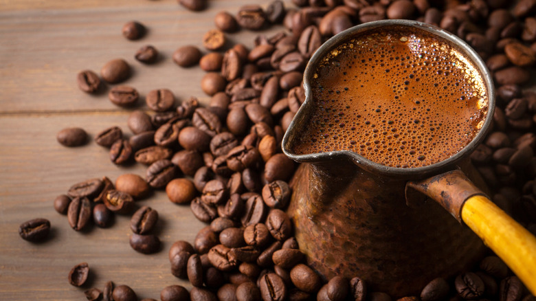 Small pot of fresh brewed coffee on a heap of coffee beans