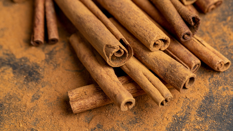 Cinnamon sticks covered in cinnamon powder on a dark surface