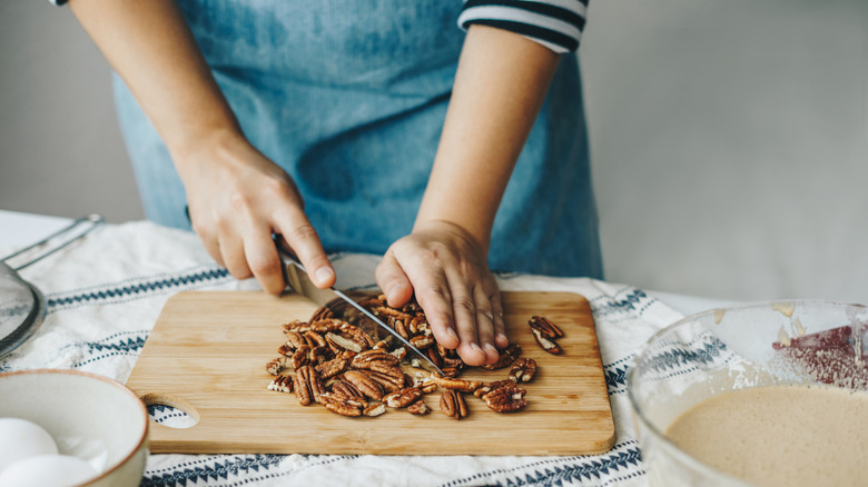 Person chopping nuts on a cutting board with batter nearby