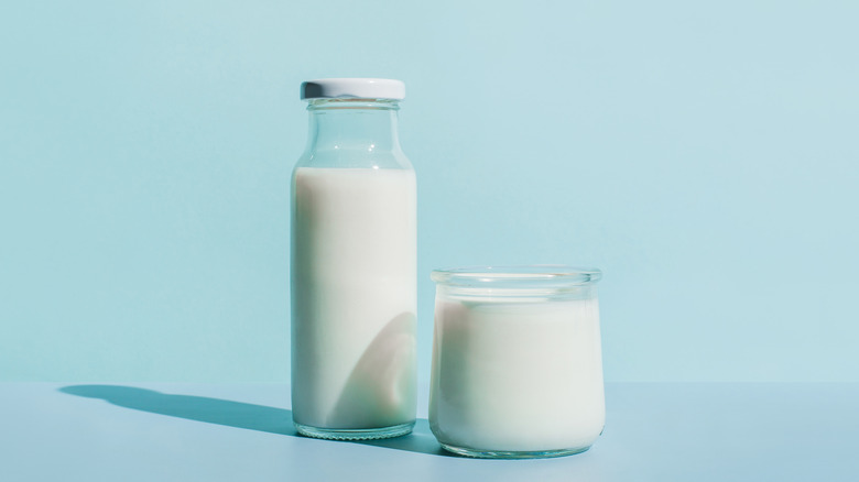 A jar of milk next to a cup of milk on a blue background