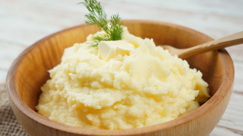 Mashed potatoes in a wooden bowl with a wooden spoon, topped with dill and butter
