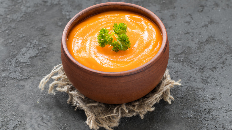 Carrot purée in a clay bowl topped with a sprig of parsley