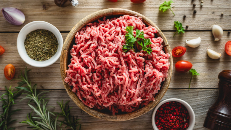 Ground beef in a wooden bowl on a wooden table surrounded by Mediterranean cooking ingredients