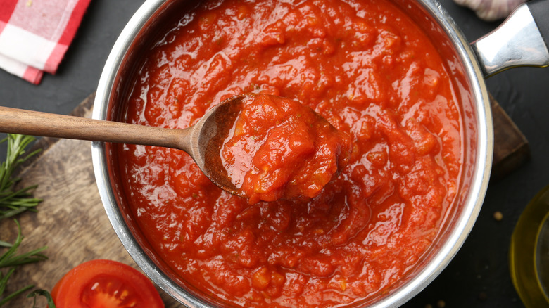 A bowl of chunky tomato sauce with a wooden spoon