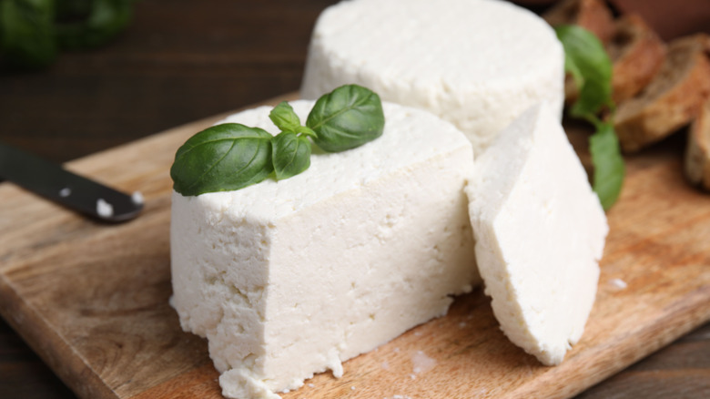 A sliced block and a whole block of ricotta cheese on a wooden board