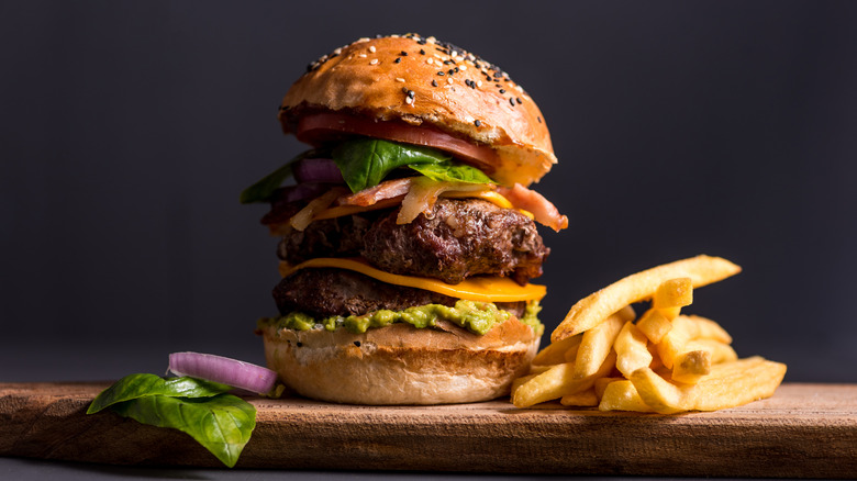 A towering burger sits next to a stack of fries
