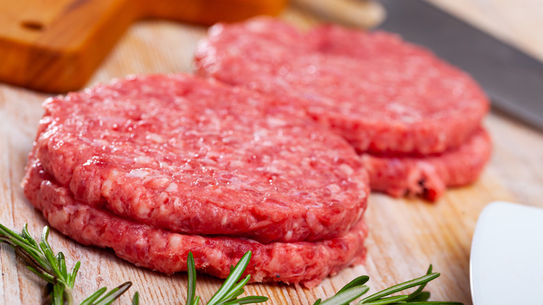 Raw burgers stacked on a wooden board