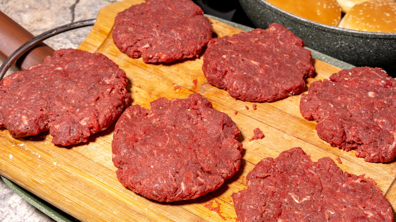 Raw burgers stacked on a wooden board, with parchment paper between each patty