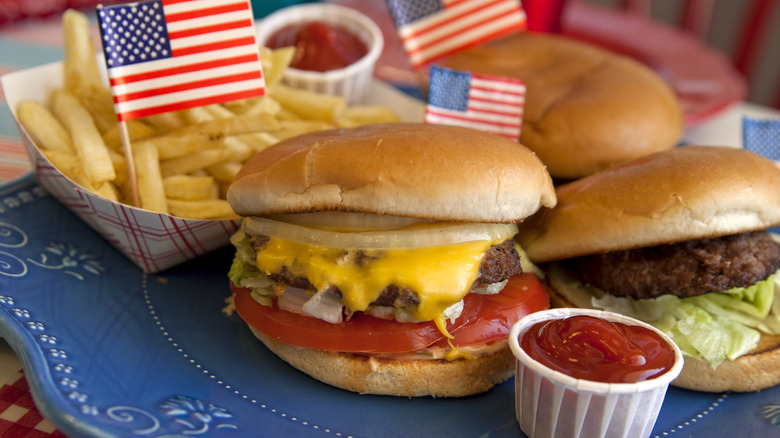Burgers, fries, and ketchup dips on a plate, with paper USA flags dotted around them