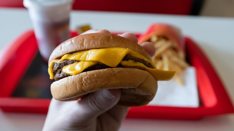 Person's hand holding a cheeseburger