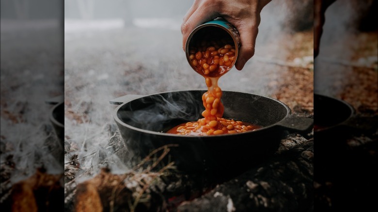 Man pouring canned beans into cast iron