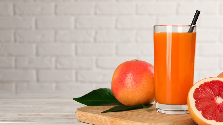Glass of grapefruit juice surrounded by whole and halved fruit
