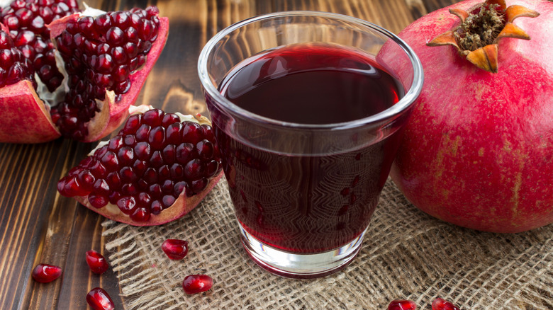 Glass of pomegranate juice surrounded by seeds and whole fruit