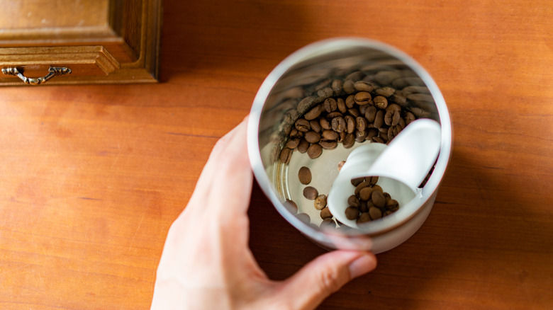 A hand holds a canister of coffee beans