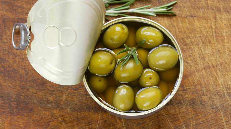 Open can of green olives, with fresh rosemary