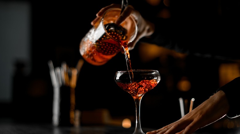 A bartender pours a cocktail into a glass