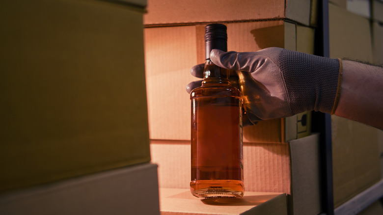 A gloved hand holds a bottle of whiskey