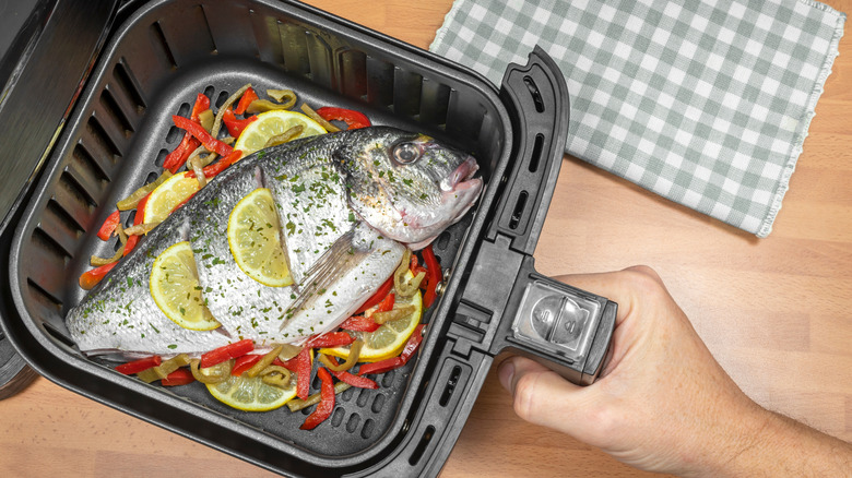 Whole fish with lemon and pepper slices in air fryer basket.